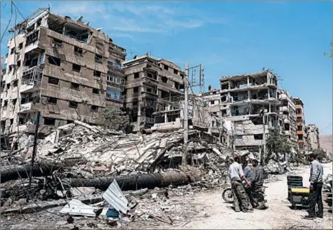  ??  ?? People stand in front of damaged buildings in Douma, Syria, near Damascus, site of a suspected chemical weapons attack last April.