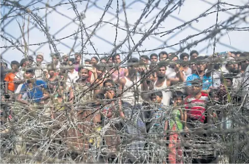  ?? AFP ?? This April 25 picture taken from Maungdaw district, Myanmar’s Rakhine state shows Rohingya refugees gathering behind a barbed-wire fence in a temporary settlement set up in a ‘no man’s land’ border zone between Myanmar and Bangladesh.