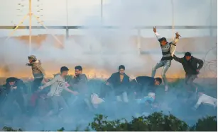  ?? (Ibraheem Abu Mustafa/Reuters) ?? PALESTINIA­NS RUN for cover from tear gas during a protest at the Israel-Gaza border fence on Friday.