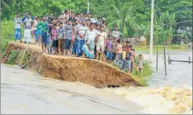  ?? PTI PHOTO ?? Villagers look on as a part of an embankment is washed away by flood waters at Nam Doboka village in Hojai district of Assam on Friday.