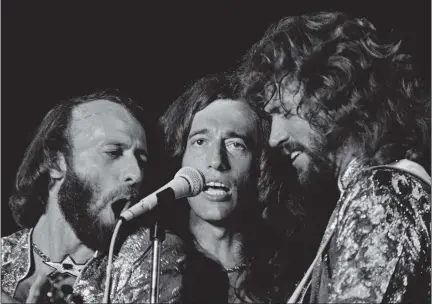  ?? PHIL SANDLIN — THE ASSOCIATED PRESS ?? Best known for some of the disco era’s most memorable songs, The Bee Gees had previously assembled a string of pop hits, many dripping with melancholy. From left, brothers Maurice, Robin and Barry Gibb share a microphone at a Miami Beach concert in 1979.