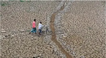  ?? — AFP photo ?? Men walk across the dry bed of a lake at Boklung village near Kathiatoli town in Nagaon District of Assam state.