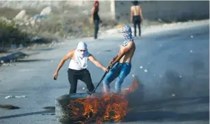  ?? (Mohamad Torokman/Reuters) ?? PALESTINIA­N PROTESTERS drag a burning tire during a protest in a-Ram, northeast of Jerusalem.