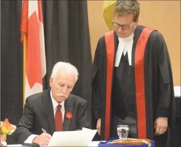  ?? MELANIE EKSAL/Penticton Herald ?? Provincial court Judge Greg Koturbash looks on as new Penticton Mayor John Vassilaki signed his oath of office Tuesday night at the inaugural meeting of the incoming city council.