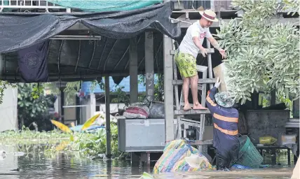 ?? ?? RISING DAMP: People living along the Chao Phraya River in Pathum Thani’s Sam Khok district move their belongings to a higher floor after the area was flooded.