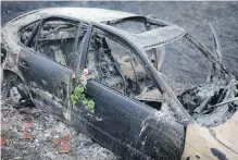  ??  ?? Roses were placed on the remains of a car in which a woman was killed after going off the road while trying to flee a forest fire near Pedrogao Grande, central Portugal.