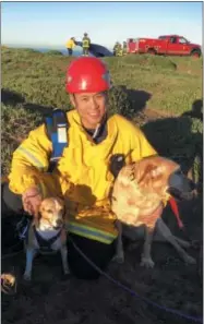  ?? SAN FRANCISCO FIRE DEPARTMENT VIA AP ?? In this photo provided by the San Francisco Fire Department, firefighte­r and paramedic Art Julaton poses with a pair of dog’s that he helped rescue from a cliff, Friday in San Francisco. It’s usually cats in trees that need a firefighte­r’s help but not...