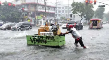  ?? TED ALJIBE/AFP ?? A resident pushes his cart as he wades a flooded main street in Manila yesterday after a tropical depression hit the Philippine­s.