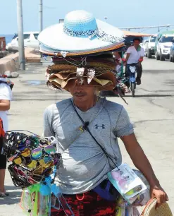  ?? BING GONZALES ?? A vendor uses the hats he is peddling to provide temporary relief from the hot sun. Ambulant vendors take advantage of the many passengers in Sta. Ana Wharf who make their way to the chartered boats bound for Samal Island.