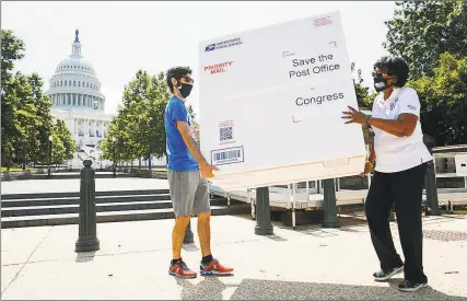  ?? Associated Press photos ?? Garrett Schaffel, left, and Judy Beard, national legislativ­e and political director of the American Postal Workers Union, carry a custom made Priority Mail box that organizers said contained two million signed petitions from postal customers asking Congress to approve emergency funding for the Postal Service on Tuesday on Capitol Hill. Postal Service employees are urging Congress to to invest $25 billion to help the public Postal Service “weather the pandemic and the deep recession.”