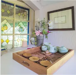  ??  ?? Left: The stained glass window connecting laundry and bathroom is a charming backdrop for a wooden tray from Afghanista­n. The tray holds a Chinese tea service and wooden plates, a gift from a family Thompson tutored. Behind is a pewter vase, with flowers from the garden, and an etching the owner created. Right: The entry features a versatile folding table and artworks, including her woodblock carving of a tree, as well as masks by carvers in Ghana and Burkina Faso, and a hand woven basket from Mali.