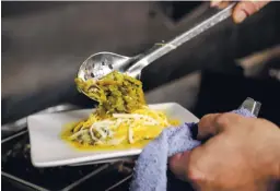  ?? PHOTOS BY GABRIELA CAMPOS THE NEW MEXICAN ?? Villarrubi­a tops a blue corn enchilada with green chile while preparing El Patron, his entry in this year’s Green Chile Cheeseburg­er Smackdown.