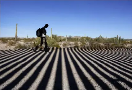  ?? Gregory Bull/Associated Press ?? A migrant walks along a road shadowed by the steel columns of the border wall separating Arizona and Mexico after crossing into the United States near Lukeville, Ariz.