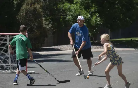  ?? Rachel Woolf, Special to The Denver Post ?? From left, Jacoby Amos, 11, his father, Brian Amos, and sister, Charlotte Amos, 9, play street hockey near their house in Littleton on Friday. But even as rinks reopen, Jacoby and his teammates from Foothills Hockey Associatio­n no longer have a home rink to return to.