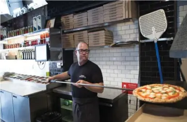  ?? NICK KOZAK PHOTOS FOR THE TORONTO STAR ?? Executive chef and partner Rocco Agostino takes a pizza out of the wood-burning oven at Pizzeria Libretto’s new location.