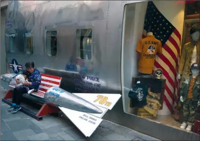  ?? The Associated Press ?? BEIJING: A woman tends to a child near a promotiona­l gimmick in the form of a bomb and the U.S. flag on April 12 outside a U.S. apparel shop in Beijing. China’s lopsided trade balance with the United States means it will run out of imports for...