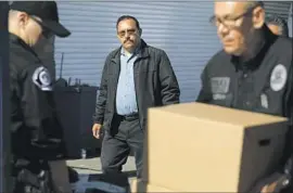  ?? Gary Coronado Los Angeles Times ?? THEN-MAYWOOD MAYOR Ramon Medina watches as L.A. County district attorney’s investigat­ors remove computers and files from his auto shop in 2018.
