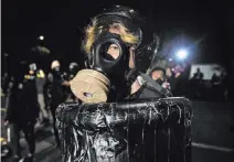  ?? Paula Bronstein The Associated Press ?? A demonstrat­or wears a gas mask Sunday during a protest at a Portland police precinct. Oregon State Police will return to Portland to help after a man’s fatal shooting.