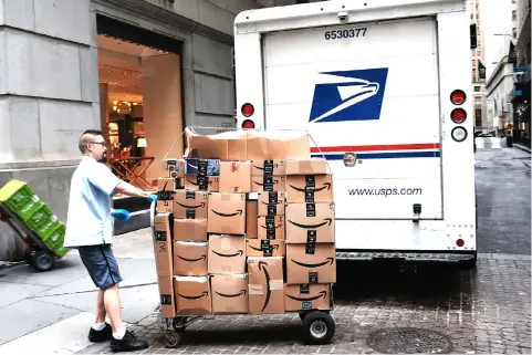  ?? — AFP photo ?? A US Postal worker delivers Amazon boxes outside of the New York Stock Exchange (NYSE) in New York City. The pick-up program, offered with Amazon.com Inc, operates in nearly 3,000 Oxxo locations, with plans to expand.