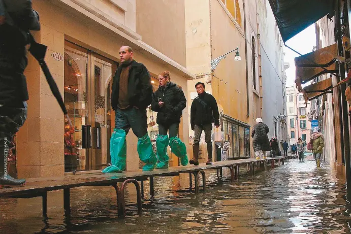  ??  ?? A la izquierda: el pabellón de Australia en la Bienal de Arquitectu­ra de Venecia, 24 de mayo de 2018Arriba: algunos turistas caminan por un distrito comercial inundado en 2005