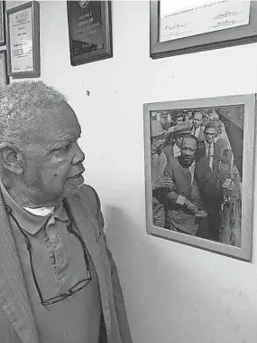  ??  ?? Fred Davis looks at a photograph of himself standing just behind Dr. Martin Luther King Jr. as they prepare to march for striking sanitation workers March 28, 1968, in Memphis.