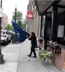  ??  ?? MAKING PREPARATIO­NS: Employee Natalia Cotirta walks with an umbrella for a table that will be placed on the sidewalk starting today at Casarecce Restorante on Hanover Street in the city’s North End.