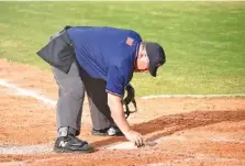  ?? STAFF PHOTO BY MATT HAMILTON ?? Umpire Ken Chase brushes off home plate in between calling balls and strikes during a baseball game at East Hamilton on March 22.