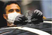  ?? Matthias Schrader / Associated Press ?? An employee attaches a Mercedes emblem to an Sclass car last month at a factory in Sindelfing­en, Germany.