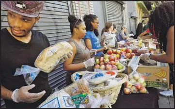  ??  ?? SAMUEL HALL, left, and other volunteers prepare to distribute groceries during the weekly food giveaway.