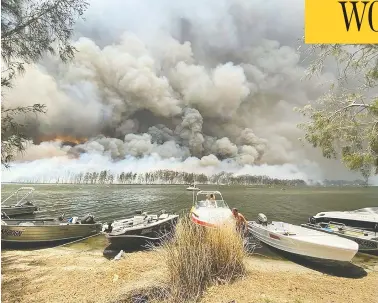  ?? ROBERT OERLEMANS VIA AP ?? Boats are pulled ashore as wildfires rage behind Lake Conjola, Australia, on Thursday. Thousands of tourists have fled Australia’s wildfire-ravaged east coast as the military started to evacuate people trapped on shore further south.