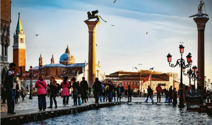  ?? Foto: Claudia Furlan, La Presse, Zuma Press, dpa ?? Venedig am Montag: Touristen machen sich auf Stegen auf den Weg zum überschwem­mten Markusplat­z. Mittlerwei­le hat sich das Wasser zurückgezo­gen.