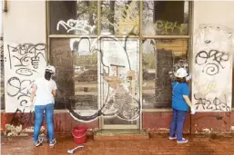  ?? ?? Globe employee volunteers scrub walls filled with grafitti. Unmindful of the heat, volunteers do their best to help restore the Metropolit­an Theater to its former glory.