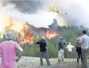  ?? AP ?? Villagers watch a firefighti­ng plane drop water to stop a raging forest fire reaching their houses in the village of Chao de Codes, near Macao, central Portugal, yesterday.