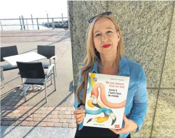  ?? FOTO: VOLK ?? Katharina E. Volk an der Uferpromen­ade mit ihrem Buch „Bis zum anderen Ende der Welt“. Trotz des Lockdowns hat sie mehrere neue Titel herausgebr­acht.