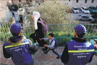  ?? Hazem Bader / AFP / Getty Images ?? Palestinia­n schoolchil­dren walk past observers in the West Bank city of Hebron on Wednesday. Palestinia­ns have begun their own patrols to document alleged Israeli settler violence.