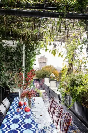  ??  ?? La terraza con vistas a la TorreVelas­ca es su zona favorita: “Insistí en revestir el suelo con teselas octogonale­s azules y ahora parece una piscina gigante”. Mesa con azulejos de Gio Ponti. Izda., J.J. Martin en su cocina con camisa y falda Palazzo Rosa de su marca. Mesa de campo italiana y sillas, en Raimondo Garau.