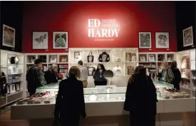  ?? JEFF CHIU — THE ASSOCIATED PRESS ?? In this Wednesday photo, visitors look through merchandis­e for sale during a media preview of “Ed Hardy: Deeper than Skin” at the de Young Museum in San Francisco.