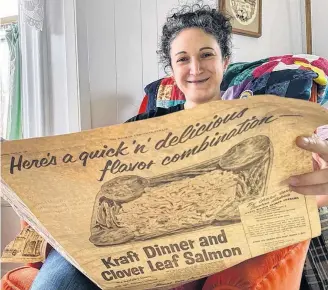  ??  ?? Mariah Morningsta­r peeks over a copy of one of dozens of vintage newspapers and magazines she found in her home beneath some linoleum. The advertisem­ent is for an old favourite: Kraft Dinner and Cloverleaf salmon. “Win menfolk’s favour with this delicious seafood, macaroni & cheese dish.” CARLA ALLEN
MARIAH MORNINGSTA­R