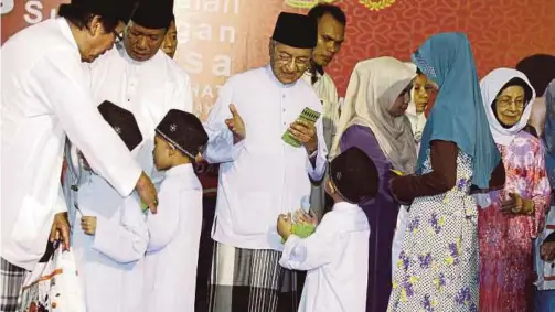  ?? PIC BY AMRAN HAMID ?? Prime Minister Tun Dr Mahathir Mohamad presenting aid to children during a breaking-of-fast event at Masjid Al Hana in Kuah, Langkawi, yesterday. With him is his wife, Tun Dr Siti Hasmah Mohamad Ali (right).