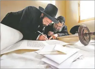  ?? Megan Avina/The Taos News ?? Rabbi Chaim Schmukler and Rabbi Y. Mishulovin of Brooklyn, N.Y. use a turkey feather from a Kosher birds’ right wing to ink in the final letters of the Torah in 2008 for the Chabad of Taos.