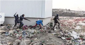  ?? — AFP photo ?? Two members of SAPS chase and shoot rubber bullets at two suspected looters outside a warehouse storing alcohol in Durban.