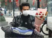  ?? ASSOCIATED PRESS ?? A man carries a Valentine’s Day bouquet Friday as he rides a scooter in Hangzhou in eastern China’s Zhejiang province. China reported another sharp rise in the number of people infected with the COVID-19 virus, as the death toll neared 1,400.