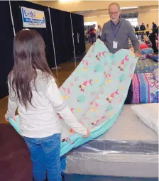  ??  ?? Volunteer Ian Palmer helps a young girl fold her new mermaid-patterned bedding at the Beds4Kids bed drive.