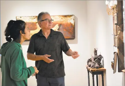  ?? Leslie Hutchison / Hearst Connecticu­t Media ?? NCCC Fine Arts major Amlisha Acosta-Silverio talks with artist Peter Brown at the opening reception of his show “Rust Forms.” The artist’s favorite piece, “Split Trunk” is on the wall behind them.