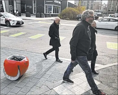  ?? Matt O’Brien The Associated Press ?? Piaggio Fast Forward CEO Greg Lynn, center, is followed by his company’s Gita carrier robot as he crosses a street in Boston. The two-wheeled machine is carrying a backpack and uses cameras and sensors to track its owner.