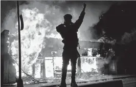  ?? JOHN MINCHILLO/AP ?? A demonstrat­or stands beside a building on fire Saturday in St. Paul, Minnesota.