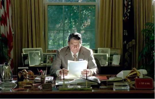  ??  ?? Above: Low autumn sunlight streams through the window behind President Reagan at his desk in the Oval Office, 1988.