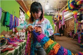  ?? Fernando Llano/Associated Press ?? Valentina Jimenez makes a traditiona­l Christmas “piñata” that will filled with fruit and candy at a family-run piñata-making business in Acolman, just north of Mexico City on Dec. 13. This style of piñata has a religious origin, with each cone representi­ng one of the seven deadly sins, and hitting the globe with a stick is a symbolic blow against sin.