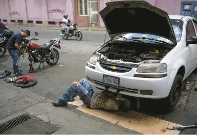  ?? MATIAS DELACROIX/AP ?? Carlos Valero repairs his car’s exhaust system last month in the San Agustin neighborho­od of Caracas, Venezuela.