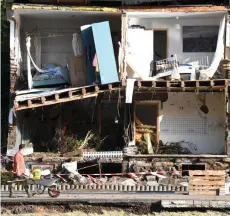  ?? — AFP photo ?? A man pushes a wheelbarro­w past a destroyed house on a muddy street full of debris in the small city of Dernau, Rhineland-Palatinate, western Germany.